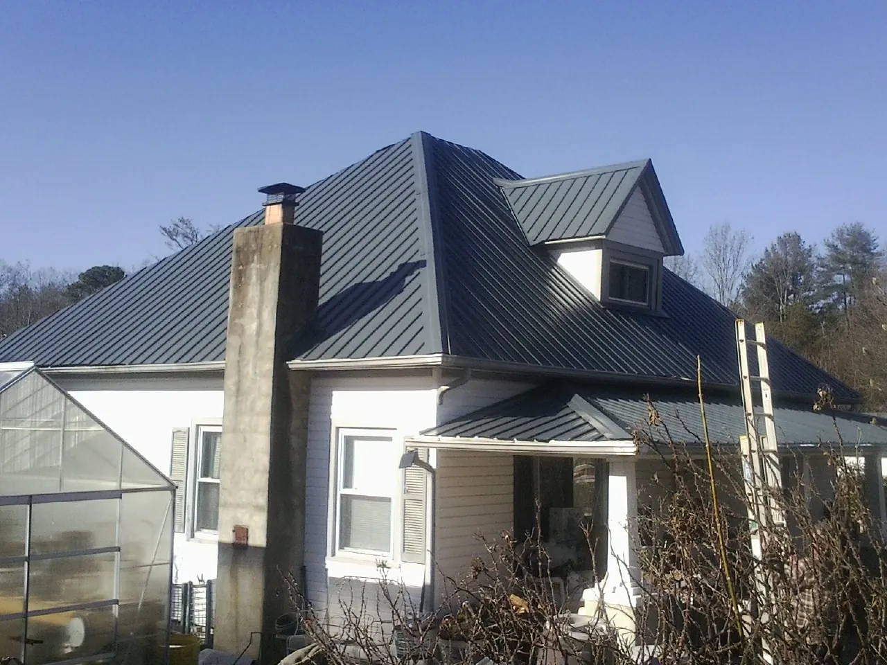 Dark blue standing seam metal roof on a white farmhouse with dormer — Slate & Tile Roof Repair by Roofing Brothers in Cutler