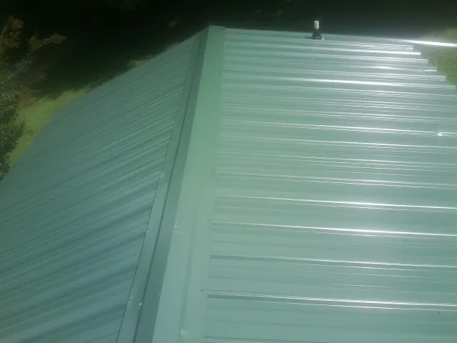 New green metal panels meeting at the ridge of a roof — Flat Roof Repair work by our crew in Cutler