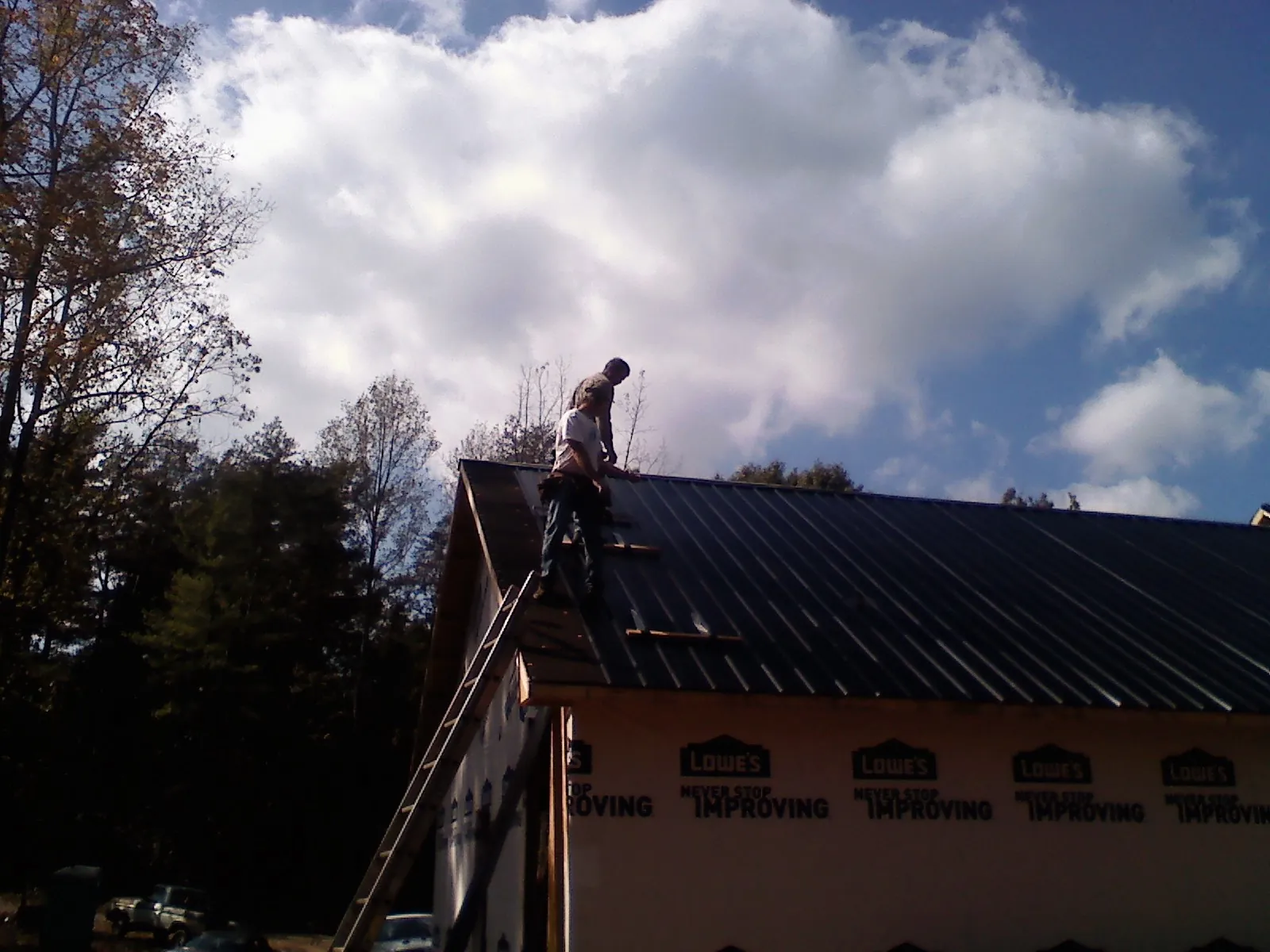Roofer fastening dark metal panels high against a cloudy sky, from a Roof Inspection job in Cutler